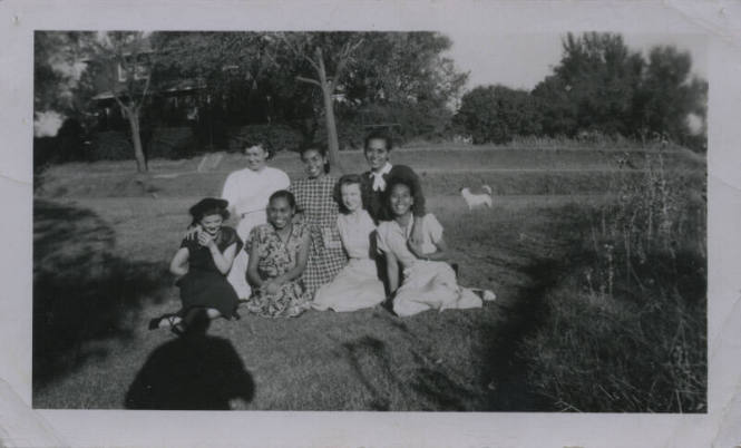 Untitled [Seven women sit on lawn, house and dog in background]