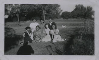 Untitled [Seven women sit on lawn, house and dog in background]