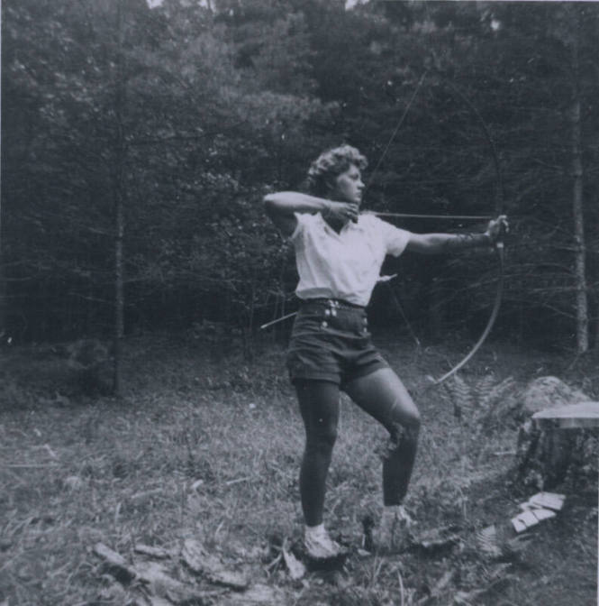 Untitled [Woman stands in forest, holds up bow and arrow]