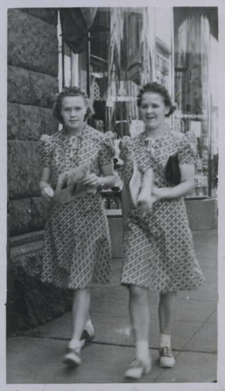 Untitled [Two women walk down street, wear matching outfits]