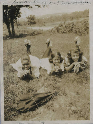 Untitled [Three women lie on grass, legs and hands crossed]