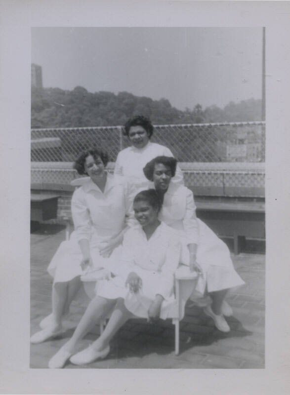 Untitled [Four women stand together, wear matching dresses and shoes]