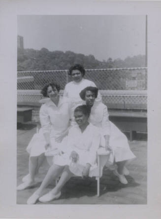 Untitled [Four women stand together, wear matching dresses and shoes]