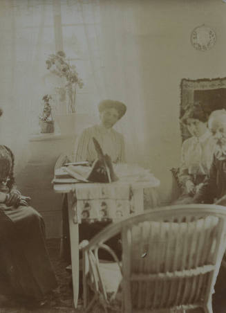Untitled [People sit around table, orchids in window]