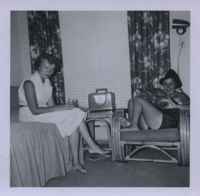 Untitled [Two women sit on bed and couch, drinks in hand]
