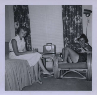 Untitled [Two women sit on bed and couch, drinks in hand]