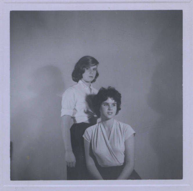 Untitled [Two women pose together, one stands, one sits and looks away, their shadows in background]