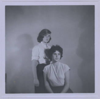 Untitled [Two women pose together, one stands, one sits and looks away, their shadows in background]
