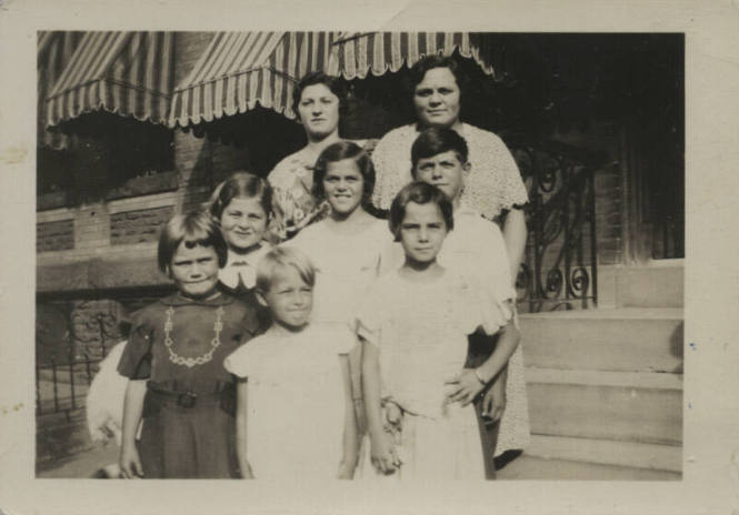 Untitled [Two women stand with six children on porch steps]