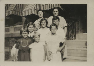 Untitled [Two women stand with six children on porch steps]