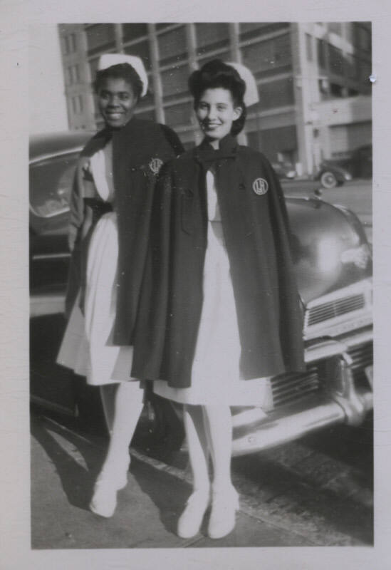 Untitled [Two women stand in front of car, wearing matching attires]