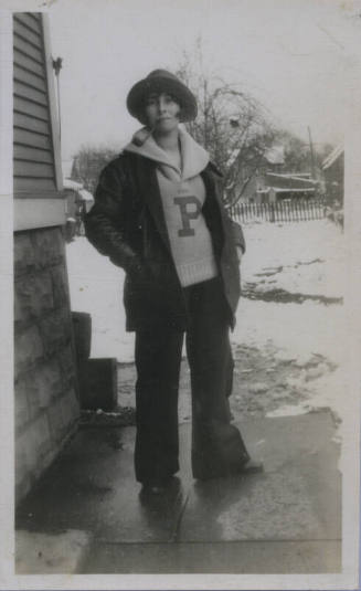 Untitled [Woman stands in snowy landscape, wears sweater with embroidered P, pipe, and coat]