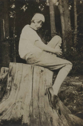 Untitled [Woman sits on tree stump, woods in background]