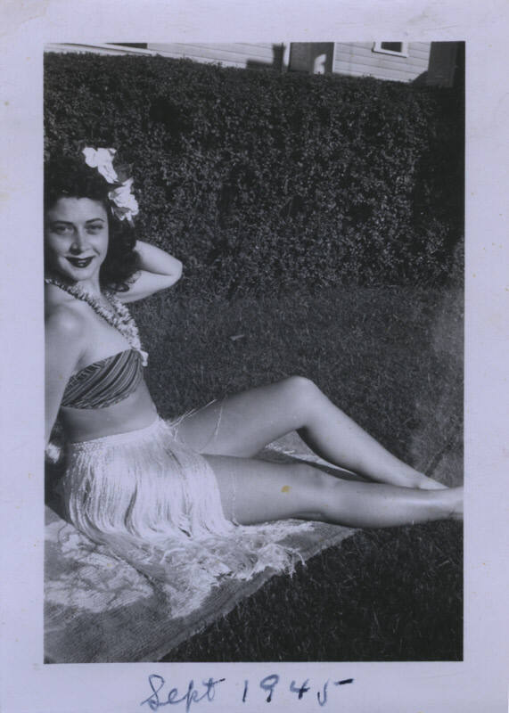 Untitled [Woman sits in towel in garden, flowers in hair and around neck]