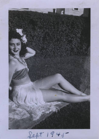 Untitled [Woman sits in towel in garden, flowers in hair and around neck]