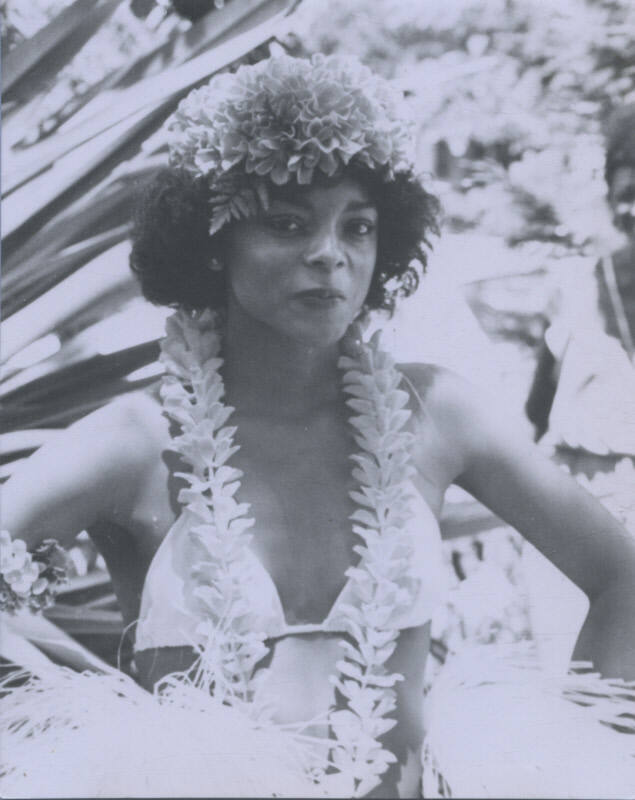 Untitled [Woman stands, hands on hips, wears flower headpiece and necklace]
