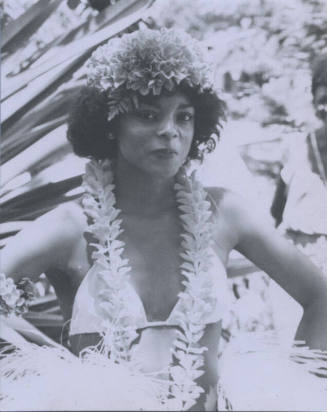 Untitled [Woman stands, hands on hips, wears flower headpiece and necklace]