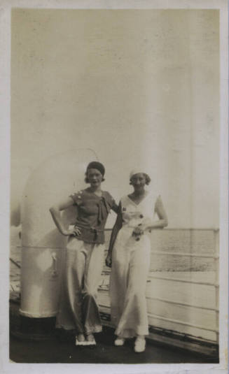 Untitled [Two women stand on deck, body of water in background]