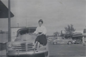 Untitled [Woman sits on car, legs crossed]