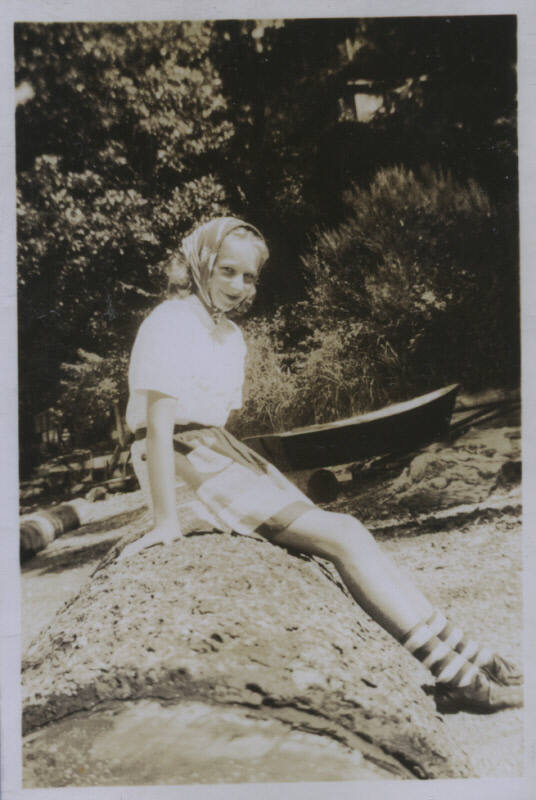 Untitled [Woman sits on rock, boat in background]