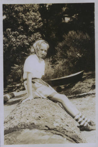 Untitled [Woman sits on rock, boat in background]