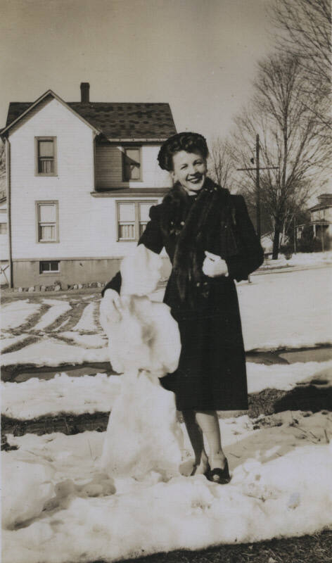 Untitled [Woman stands next to snowman]