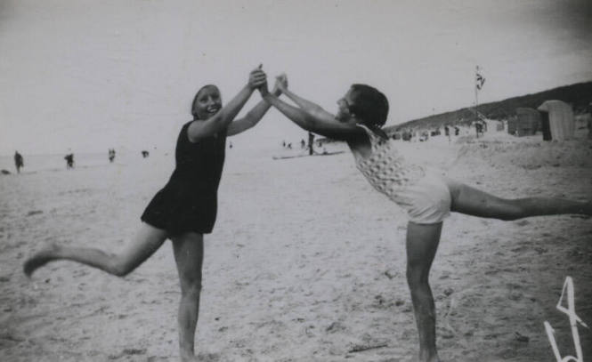 Untitled [Two women hold hands and stand on one leg in beach]