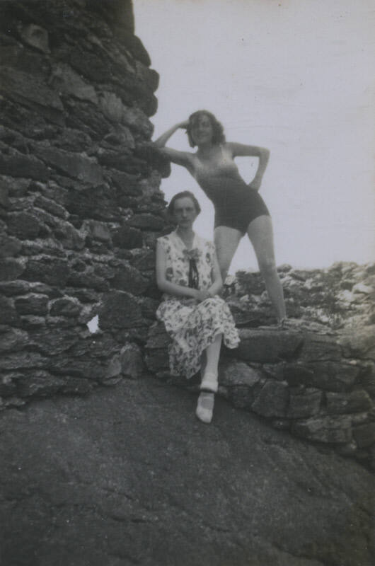 Untitled [Two women sit and stand on rock wall and ledge]