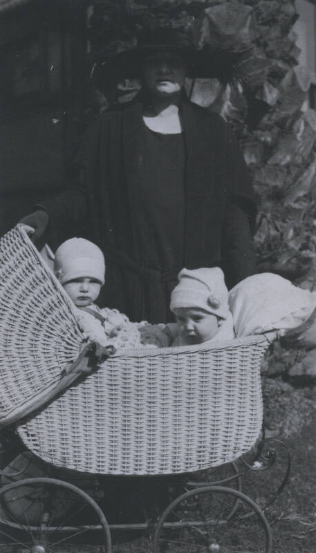 Untitled [Woman stands with stroller, two children inside]