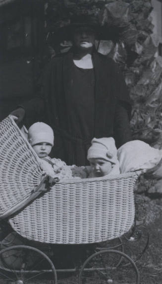 Untitled [Woman stands with stroller, two children inside]