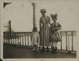 Untitled [Woman stands with two children, leans on rail]