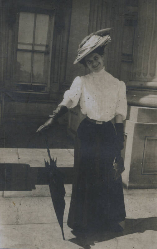Untitled [Woman stands on street, balances umbrella with one hand]
