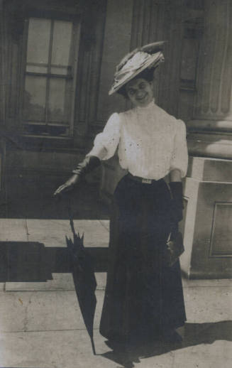 Untitled [Woman stands on street, balances umbrella with one hand]