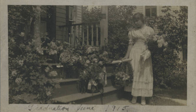 Untitled [Woman stands on porch, holds flowers]