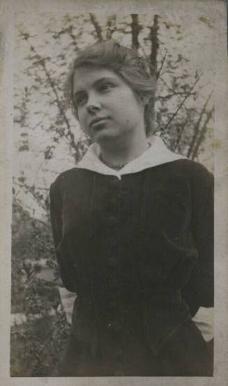 Untitled [Woman stands outdoors, looks at something unpictured]