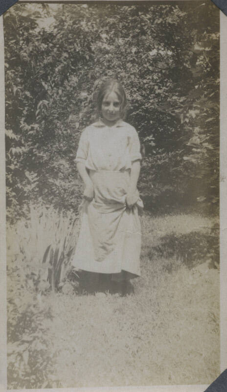 Untitled [Woman stands on garden, holds up skirt]