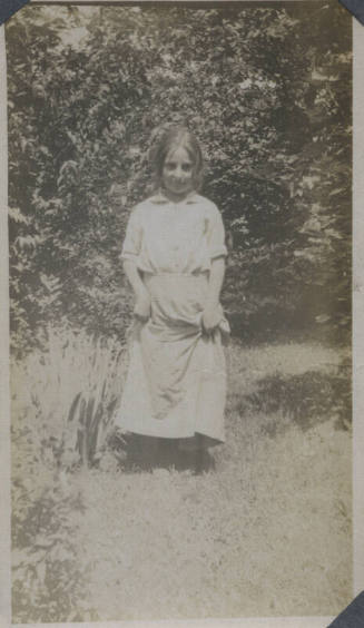 Untitled [Woman stands on garden, holds up skirt]