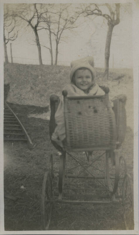 Untitled [Child sits on stroller, trees in background]