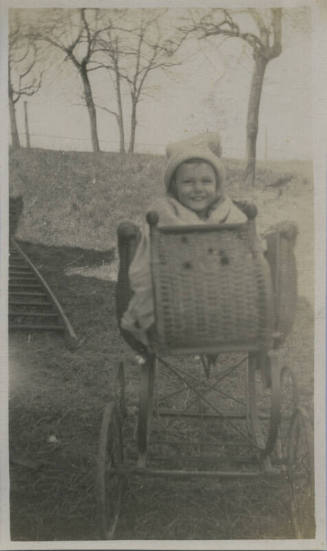 Untitled [Child sits on stroller, trees in background]