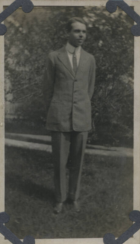 Untitled [Man stands in garden, hands behind back, looks away]