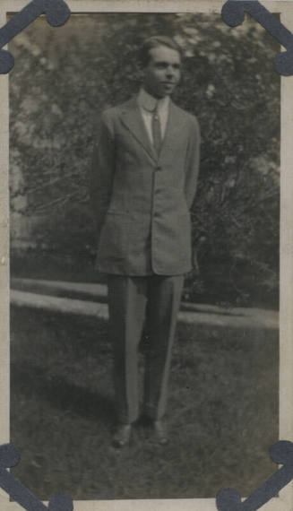 Untitled [Man stands in garden, hands behind back, looks away]