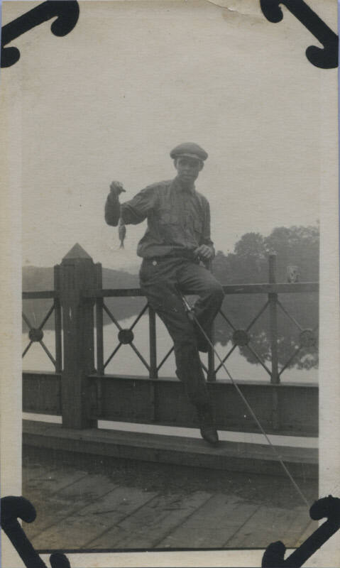 Untitled [Man sits on rail, holds up fish]