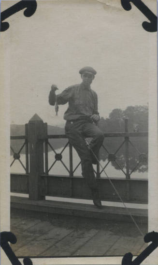 Untitled [Man sits on rail, holds up fish]