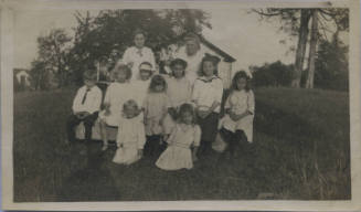 Untitled [Two women stand with nine children, house in backgrond]