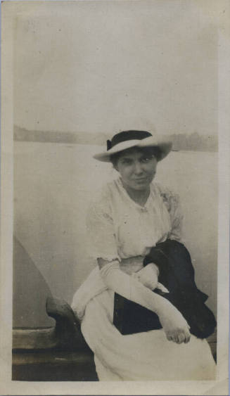 Untitled [Woman wears gloves and hat, body of water in background]