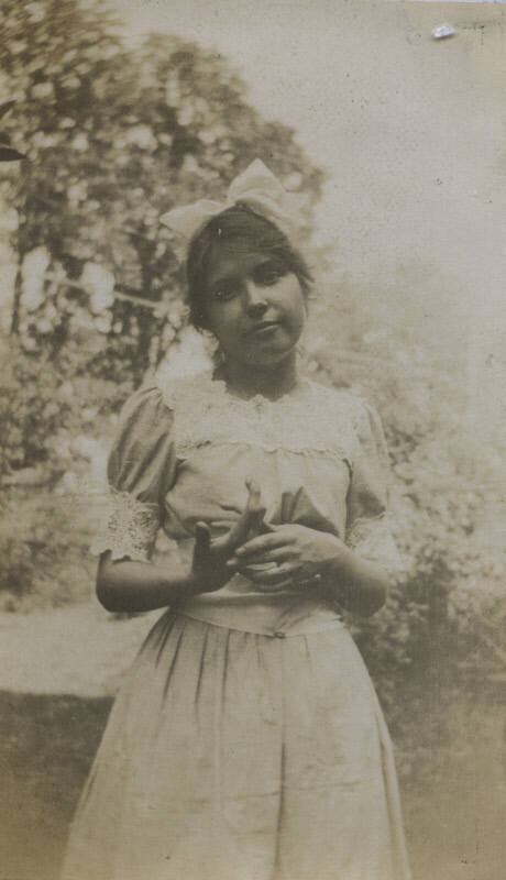 Untitled [Woman stands in garden, wears bow]