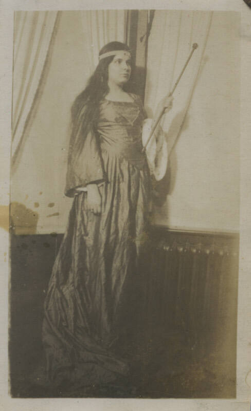 Untitled [Woman stands indoors, wears gown and holds stick]
