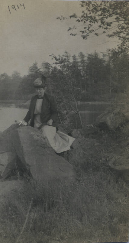 Untitled [Woman stands among rocks, body of water in background]