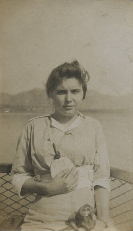 Untitled [Woman holds bag and fan, body of water in background]