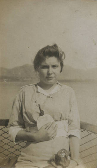 Untitled [Woman holds bag and fan, body of water in background]